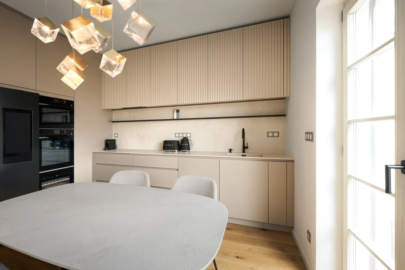 Kuchyňská linka na míru v matném pískovém odstínu s jídelním stolem a designovým lustrem